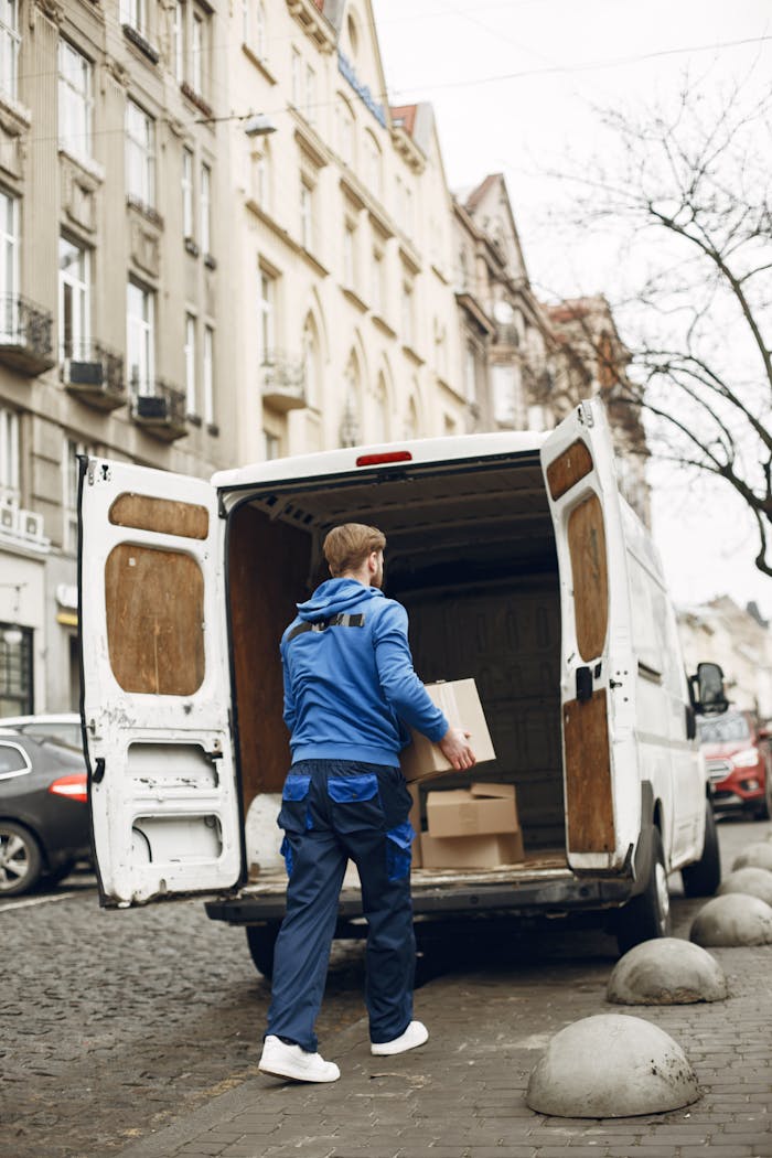 A delivery person loads boxes into a van on a cobblestone street, showcasing urban logistics.